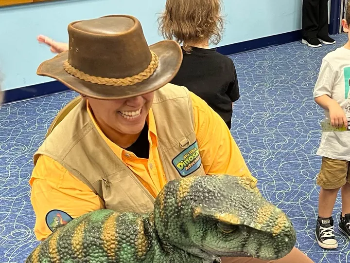 A Dinosaur Trainer holds a baby dinosaur puppet in a program room