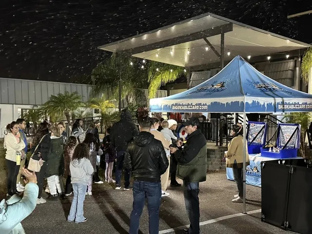 Families gather at night under string lights as artificial snow falls over winter games