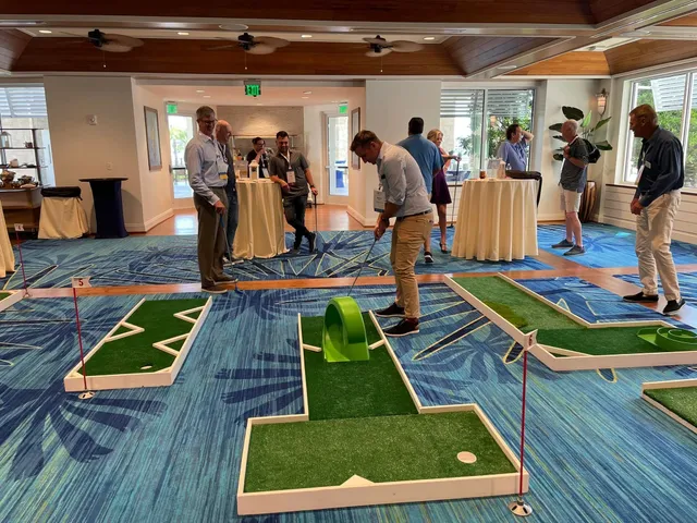 Conference guests with name badges play a portable mini golf course set up in an event room