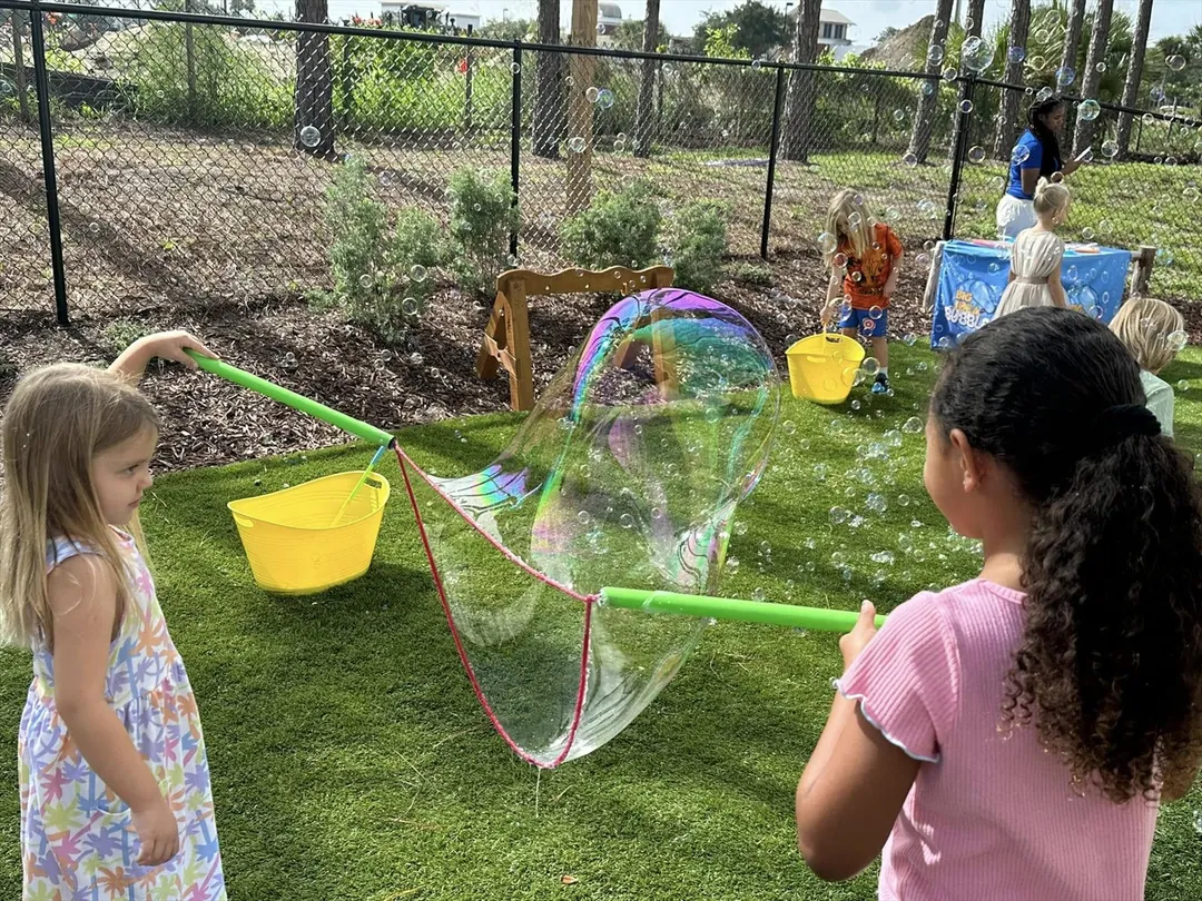 Two girls stretch a giant rainbow bubble between their wands