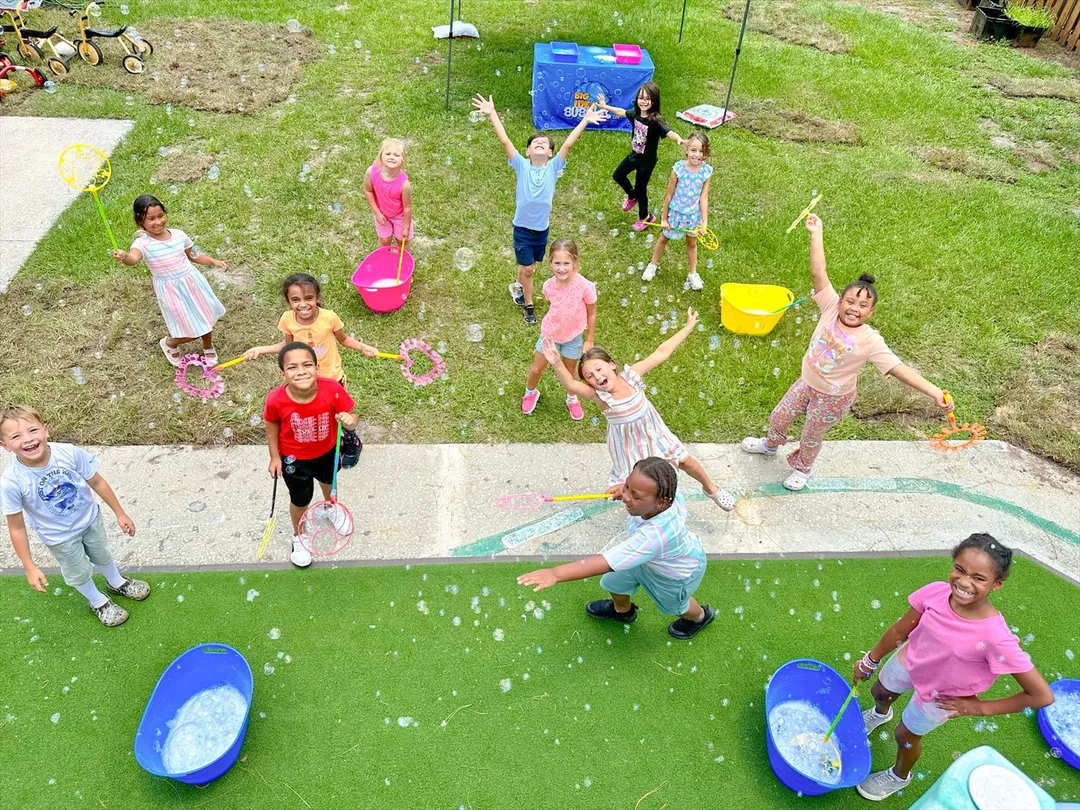 A group of kids cheer with bubble wands as bubbles float around them