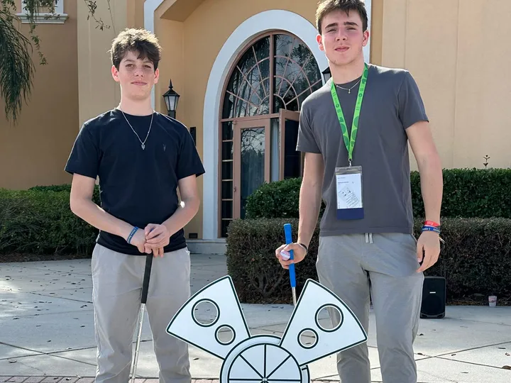 Two young adults with event lanyards stand with putters beside a portable mini golf hole