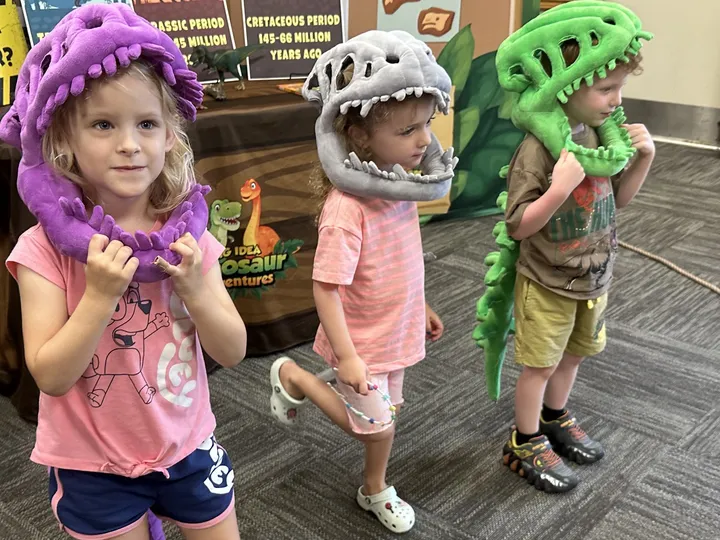 Preschoolers in plush dinosaur hats pose during an indoor program