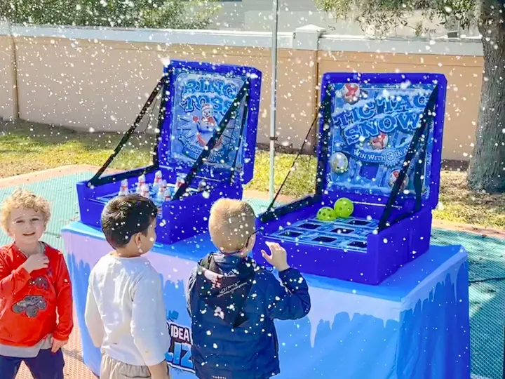 Kids play snow-themed carnival games under a canopy as artificial snow falls