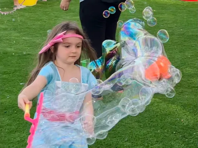 A girl pulls a giant bubble wand across a lawn