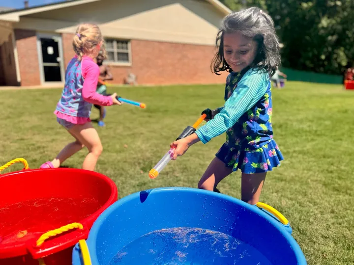 Kids fill water blasters from buckets on a sunny lawn
