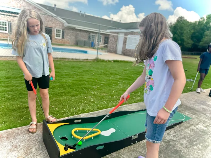 Two girls putt on a portable mini golf hole in a backyard