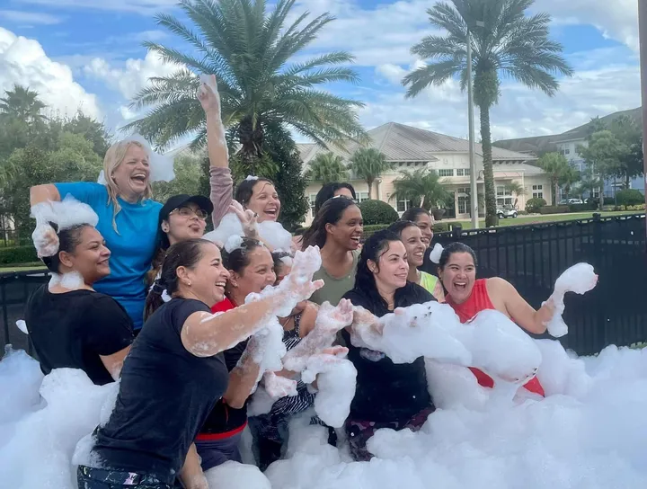 A group of adults celebrating together in foam at an outdoor team event